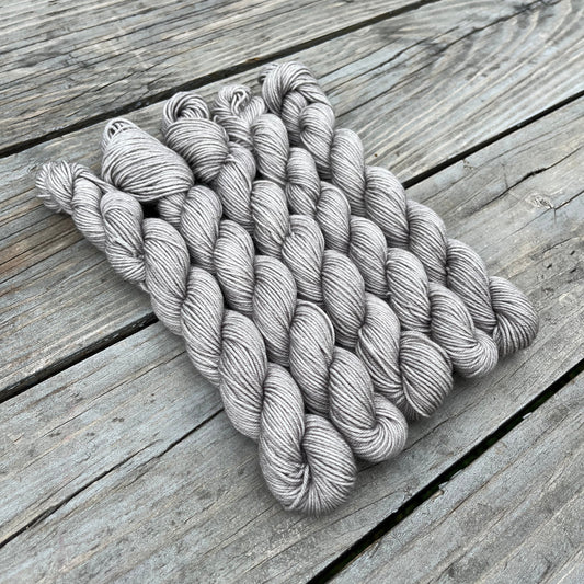 5 skeins of gray yarn on a wooden table.
